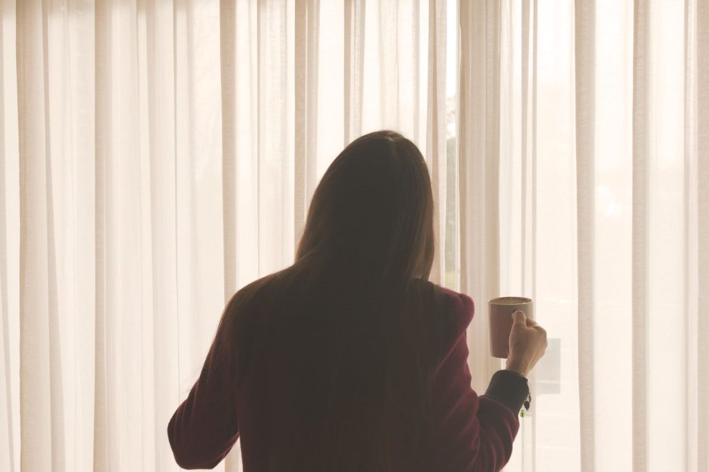 Giselle is drinking coffee and looking out the window, with the afternoon sunlight filtering through the window's curtains.