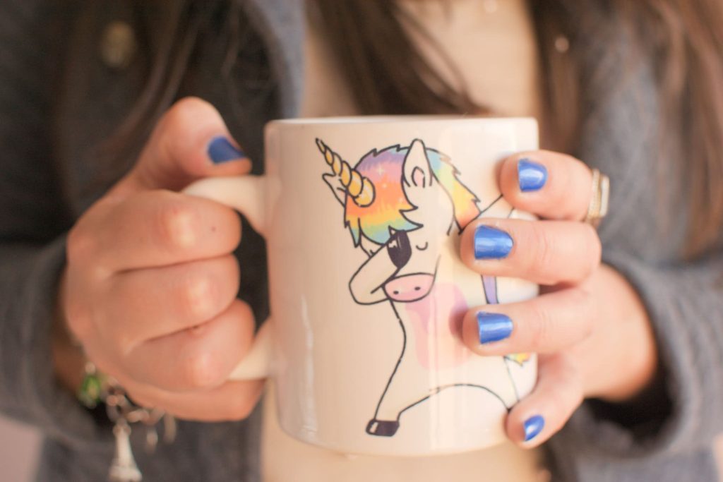 Giselle is holding a mug with a drawing of a unicorn gently slapping its forehead.