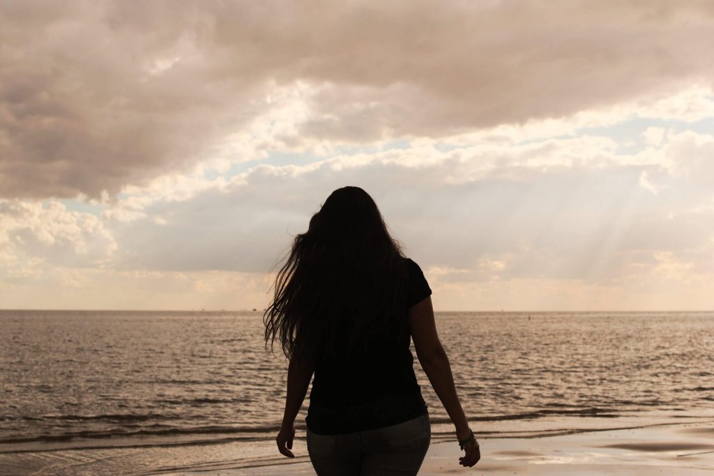 Giselle’s silhouette on a cloudy sunset, in front of the Río De La Plata in Colonia. In the background, there are crepuscular rays filtering through the clouds.