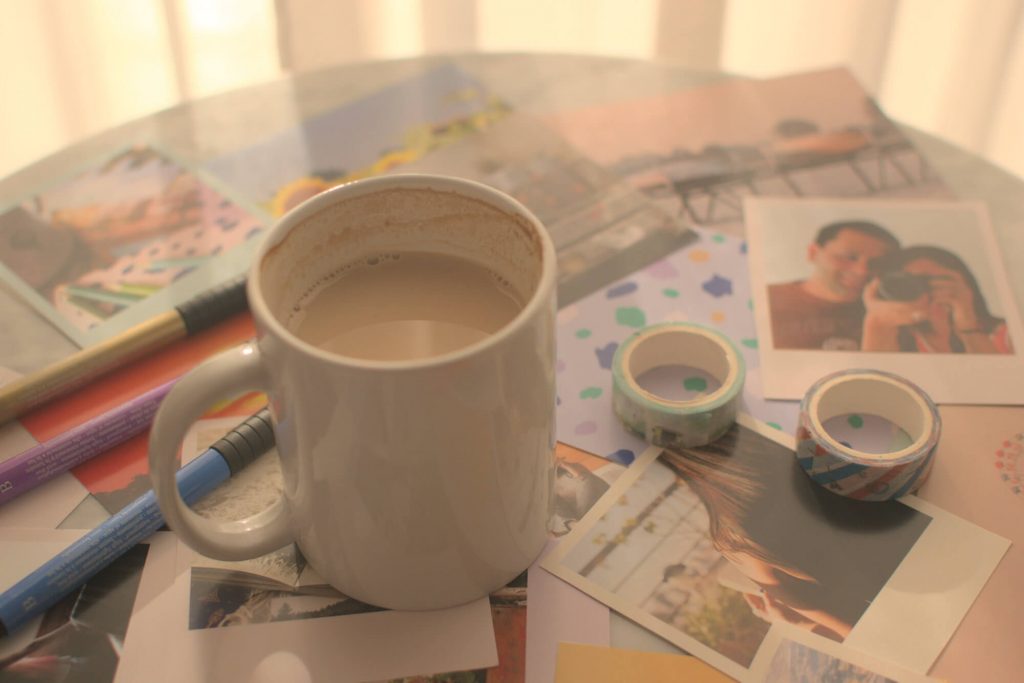Washi tapes, coffee mug, brush pens, and printed photos, over a marble coffee table, in the afternoon light filtering through the curtains.